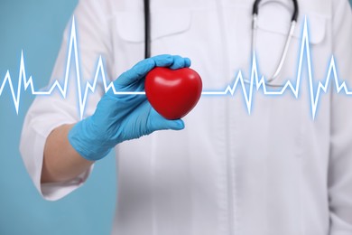 Image of Doctor holding red heart on light blue background, closeup 