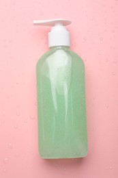 Photo of Wet bottle of face cleansing product on pink background, top view