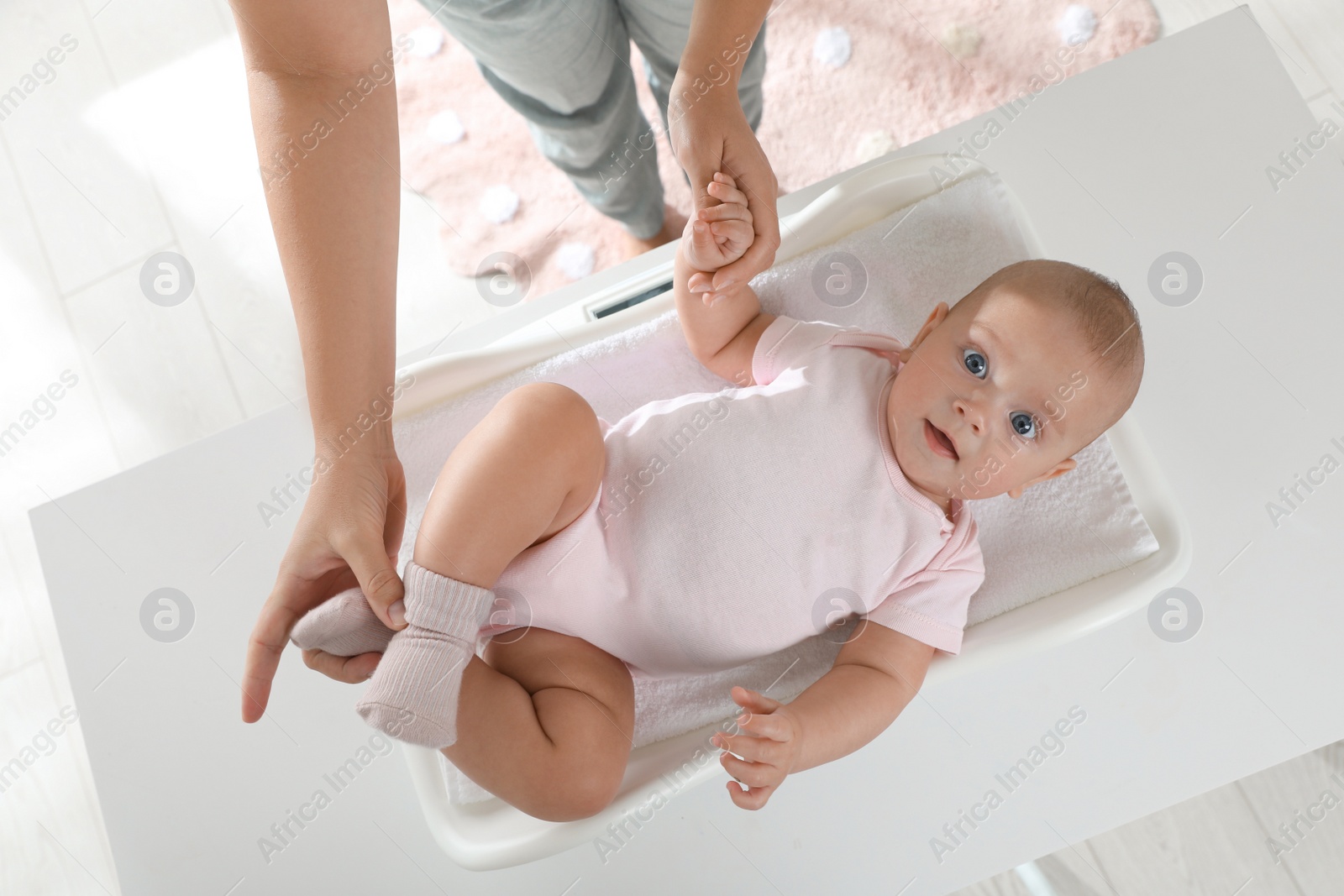 Photo of Young woman weighting her cute baby at home, top view. Health care