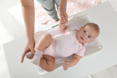 Photo of Young woman weighting her cute baby at home, top view. Health care