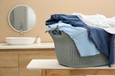 Photo of Plastic laundry basket overfilled with clothes on white table in bathroom. Space for text