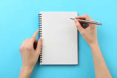 Photo of Woman writing in notebook on light blue background, top view