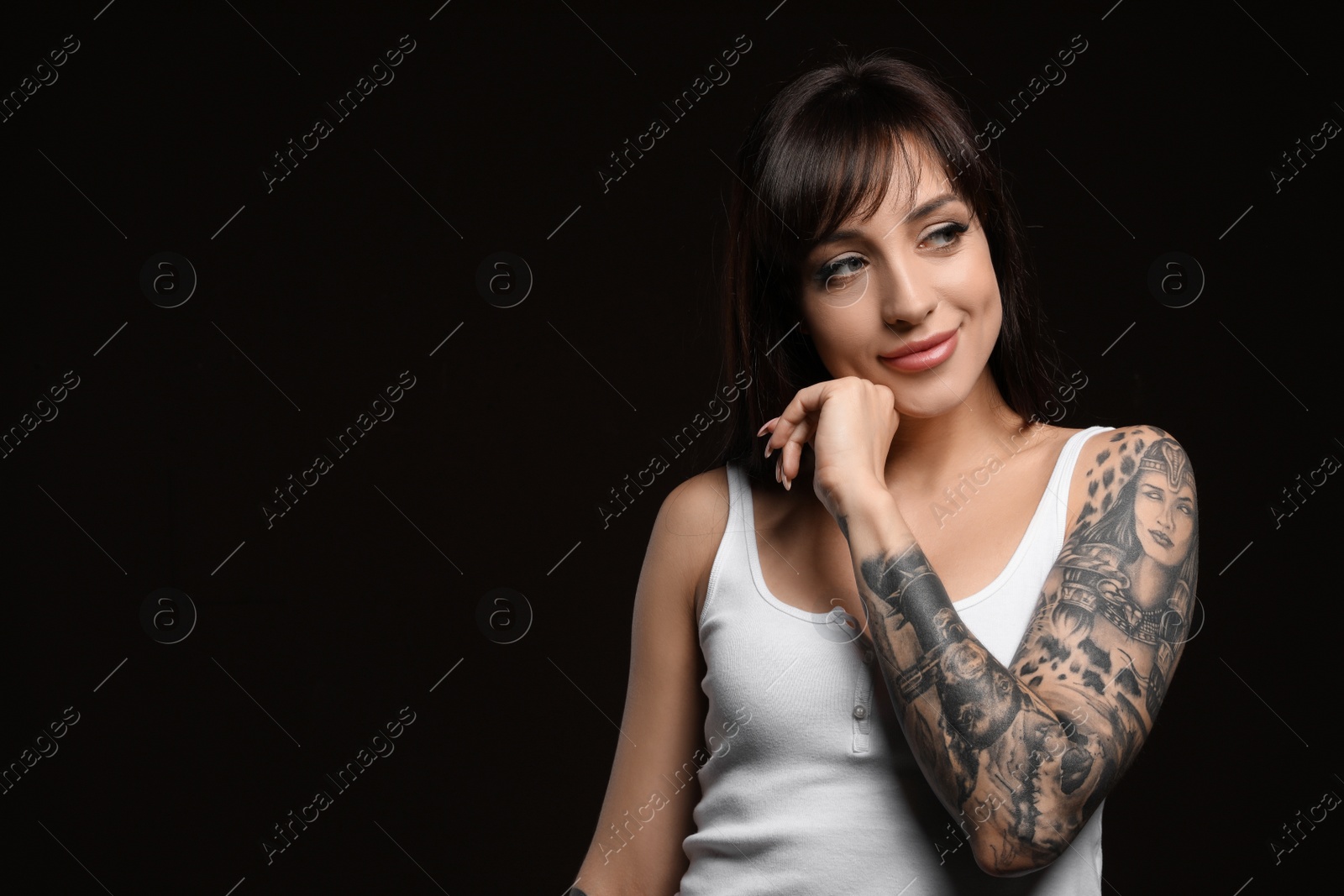 Photo of Beautiful woman with tattoos on arm against black background. Space for text