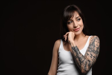 Photo of Beautiful woman with tattoos on arm against black background. Space for text