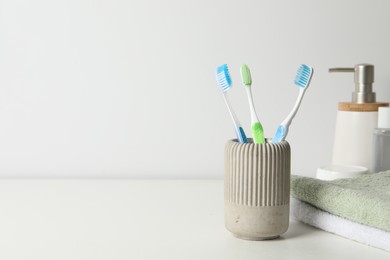 Photo of Plastic toothbrushes in holder, towels and cosmetic products on white countertop, space for text