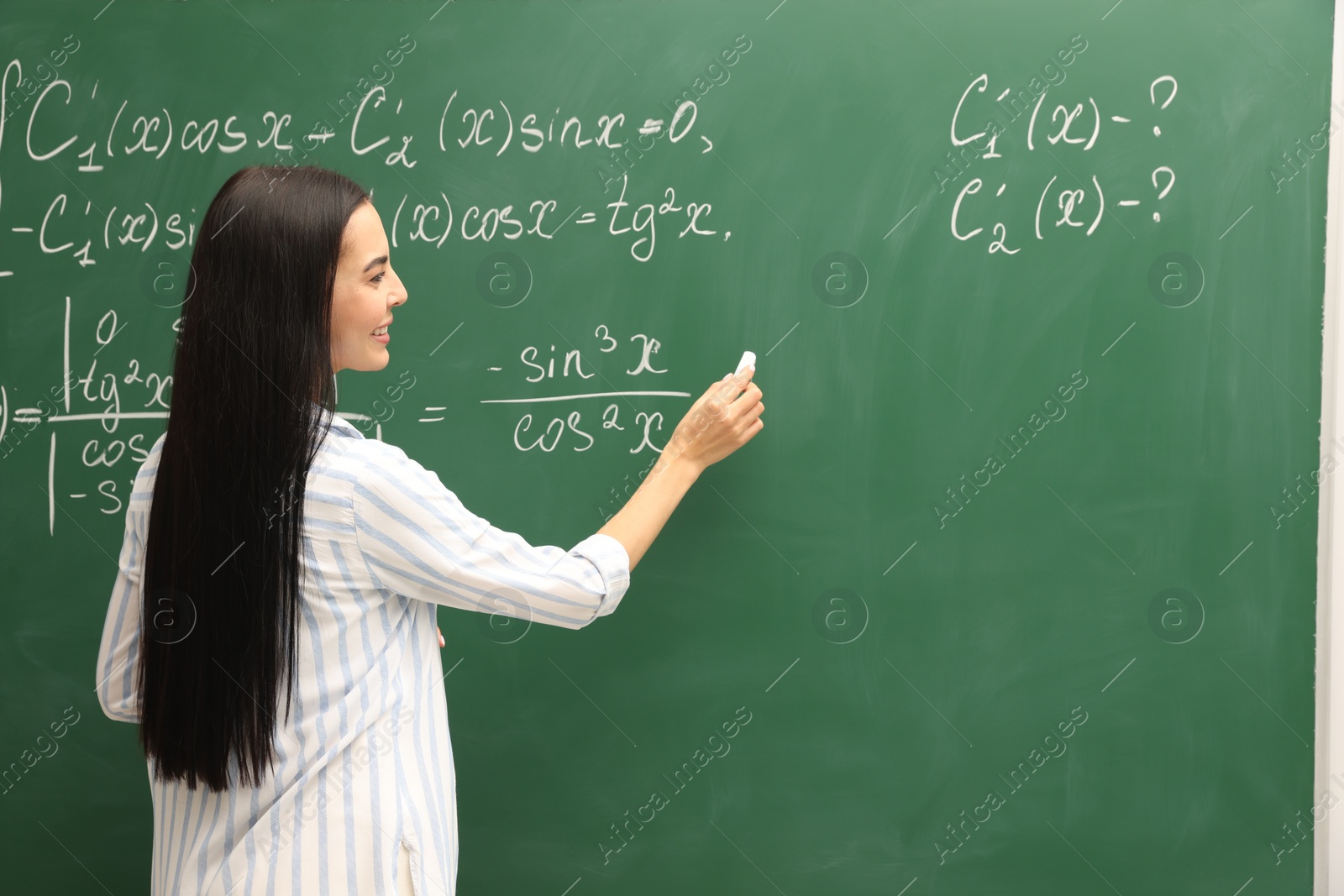 Photo of Happy teacher explaining mathematics at chalkboard in classroom