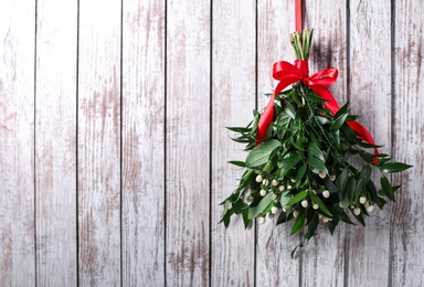 Mistletoe bunch with red bow hanging on white wooden wall, space for text. Traditional Christmas decor