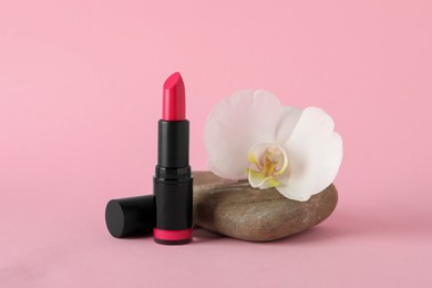 Photo of Beautiful lipstick and orchid flower on stone against pink background