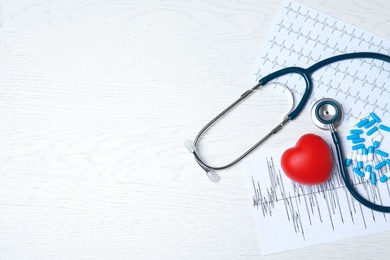 Photo of Medical stethoscope, heart, pills and cardiograms on wooden background, top view with space for text. Cardiology concept