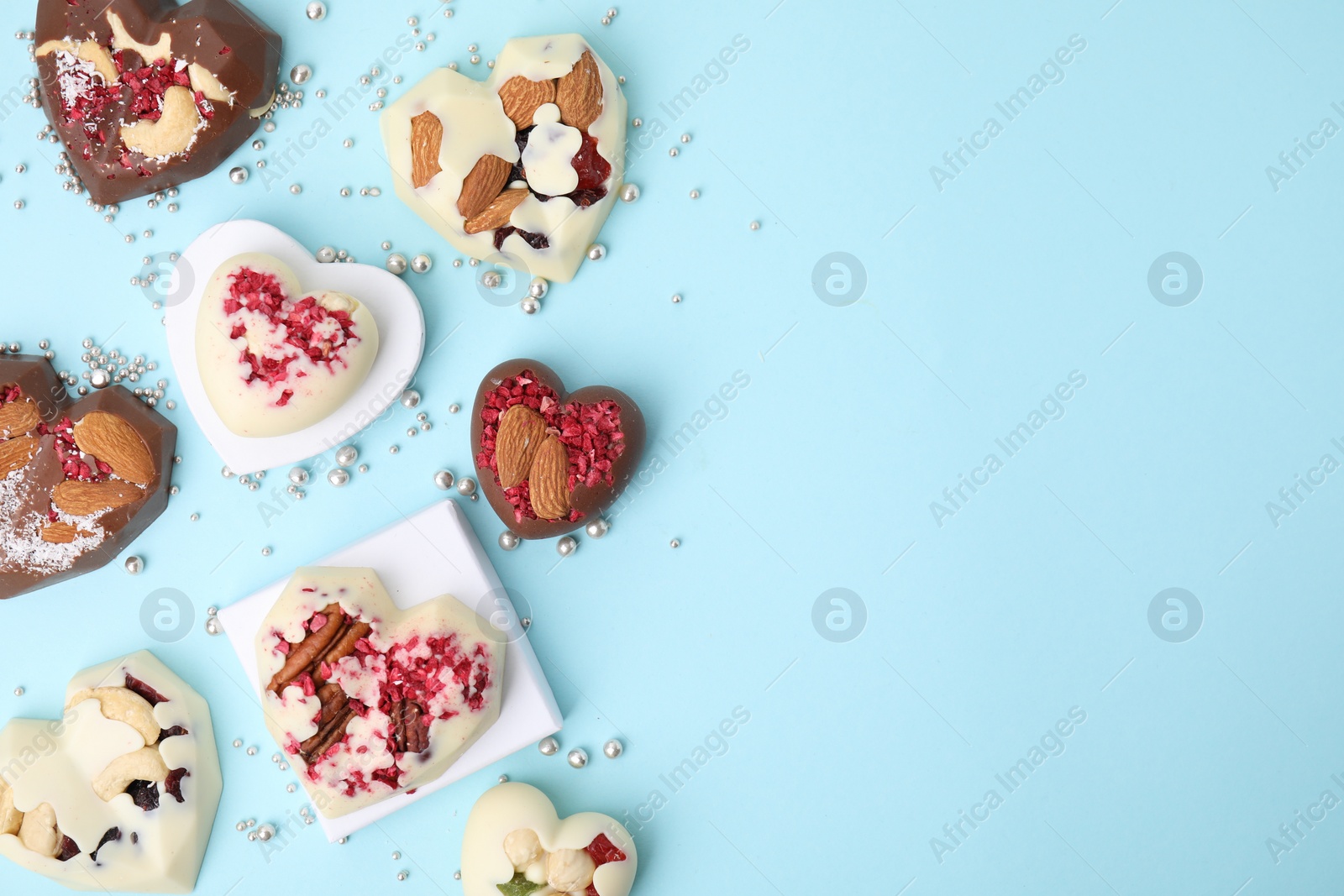 Photo of Tasty chocolate heart shaped candies with nuts on light blue background, flat lay. Space for text