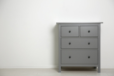 Grey chest of drawers near light wall. Space for text