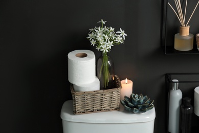 Decor elements, necessities and toilet bowl near black wall. Bathroom interior