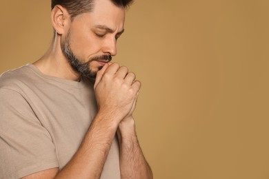 Photo of Man with clasped hands praying on beige background. Space for text