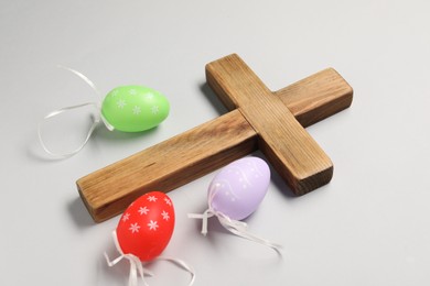 Wooden cross and painted Easter eggs on light grey background