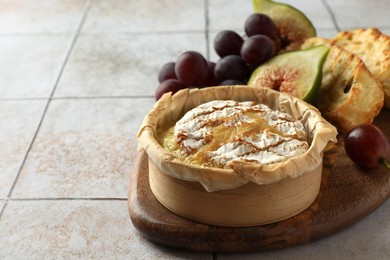 Photo of Tasty baked brie cheese and products on light tiled table, closeup. Space for text