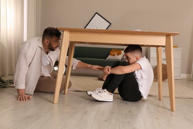 Photo of Father comforting his scared son under table in living room during earthquake