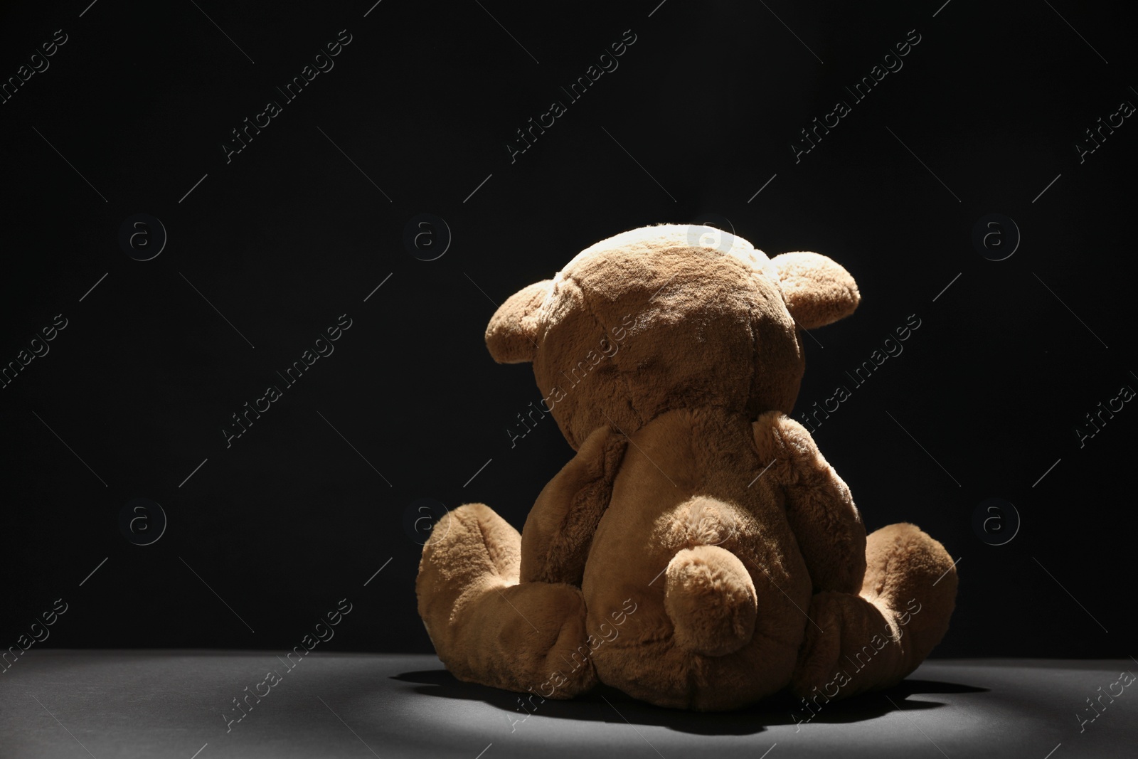 Photo of Cute lonely teddy bear on dark background, back view. Space for text
