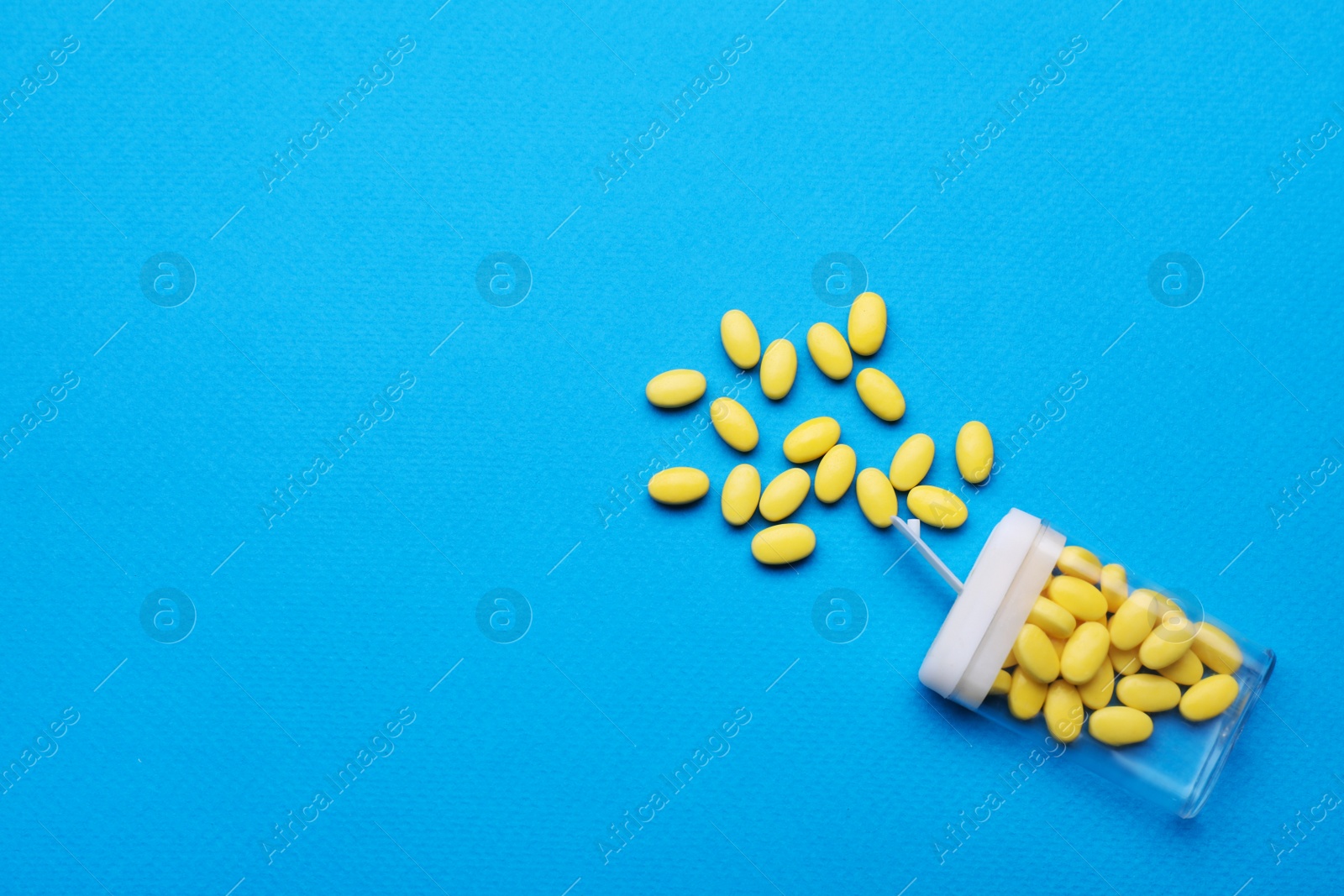 Photo of Tasty yellow dragee candies and container on blue background, flat lay. Space for text