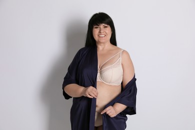 Photo of Beautiful overweight woman in beige underwear and silk robe on light background. Plus-size model