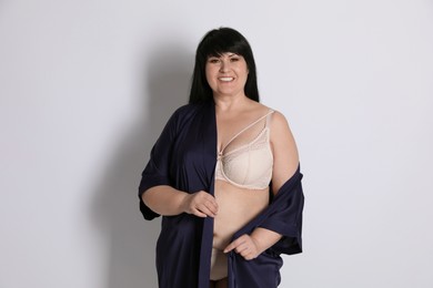 Beautiful overweight woman in beige underwear and silk robe on light background. Plus-size model