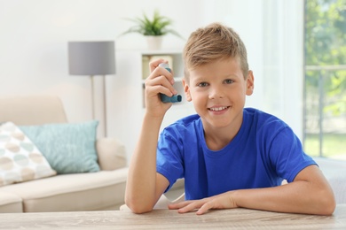 Photo of Little boy with asthma inhaler at table indoors