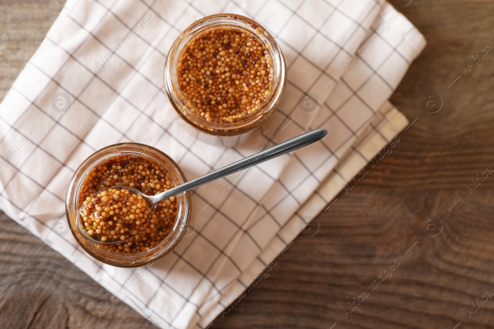 Photo of Jars and spoon of whole grain mustard on wooden table, flat lay. Space for text