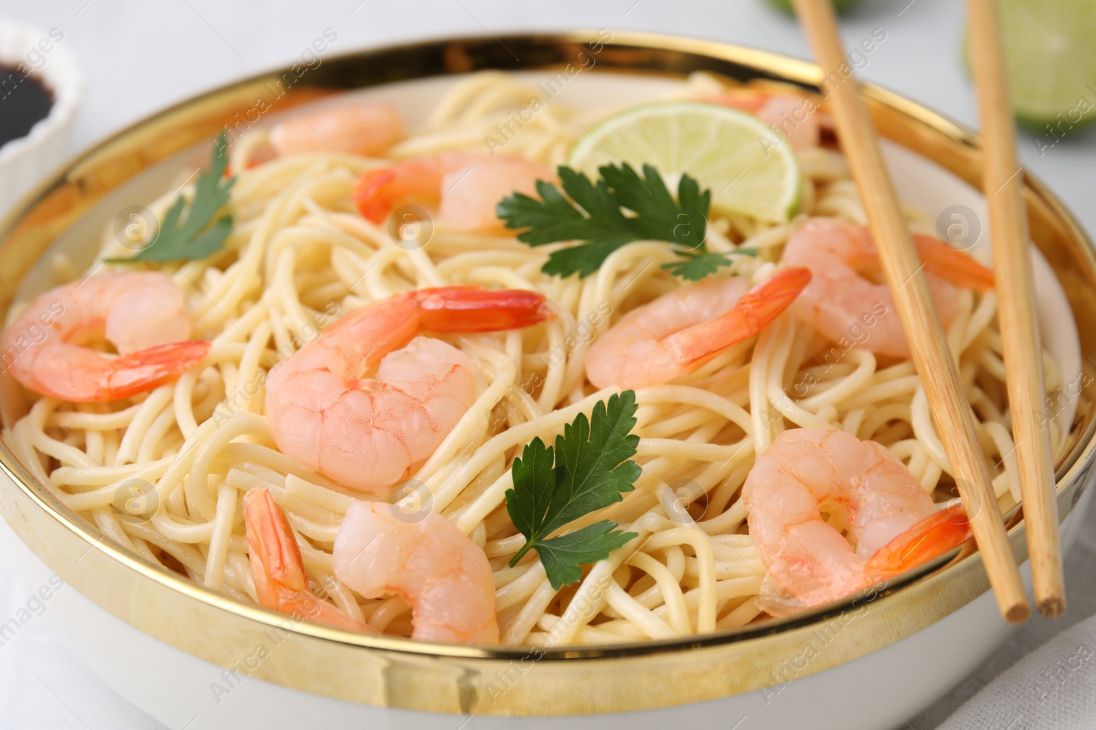 Photo of Tasty spaghetti with shrimps, lime and parsley in bowl on white table, closeup