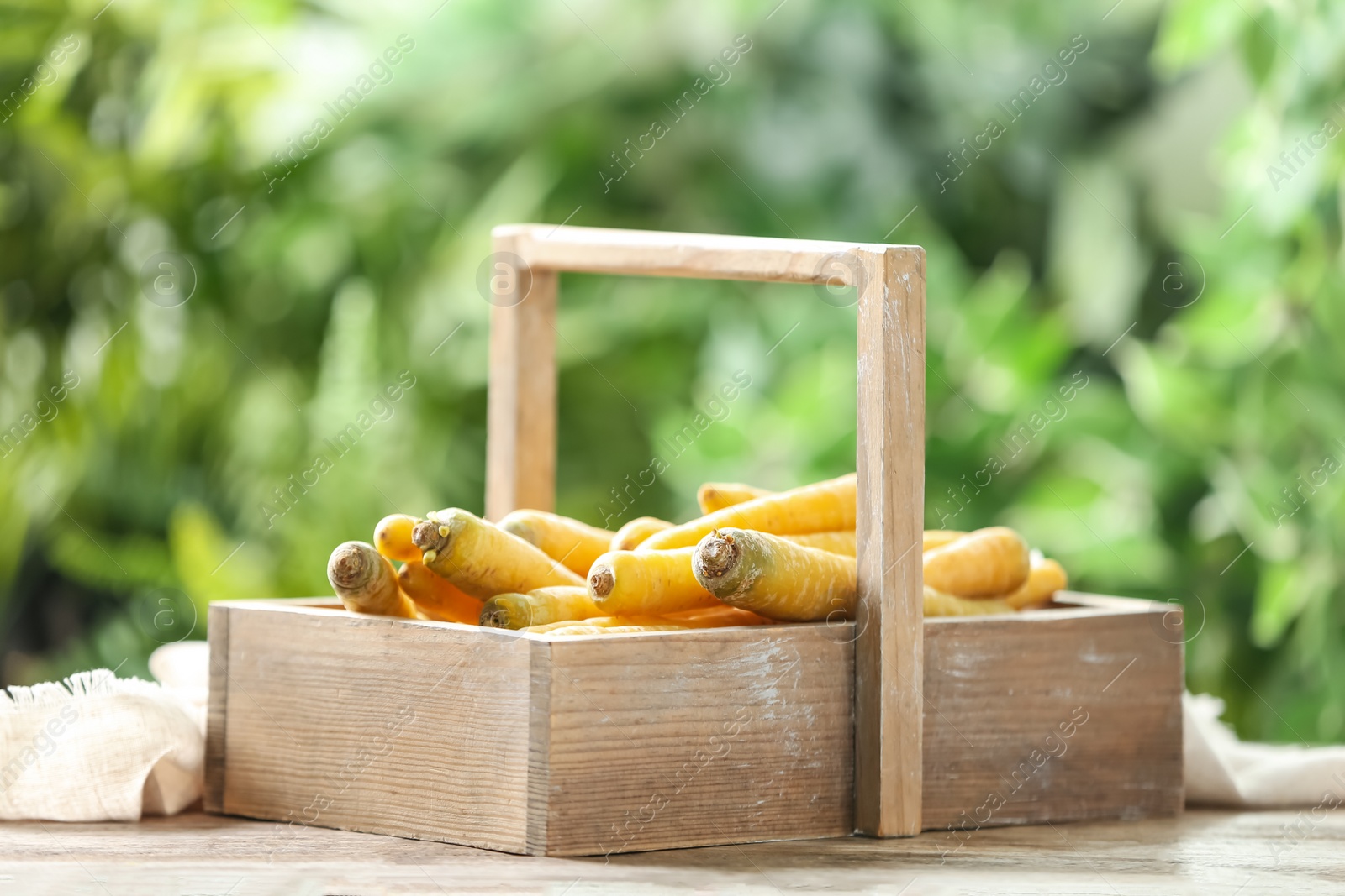 Photo of Raw yellow carrots in wooden basket on table against blurred background