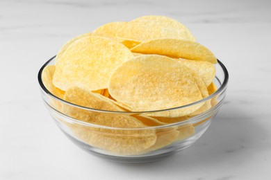 Bowl with delicious potato chips on white marble table, closeup