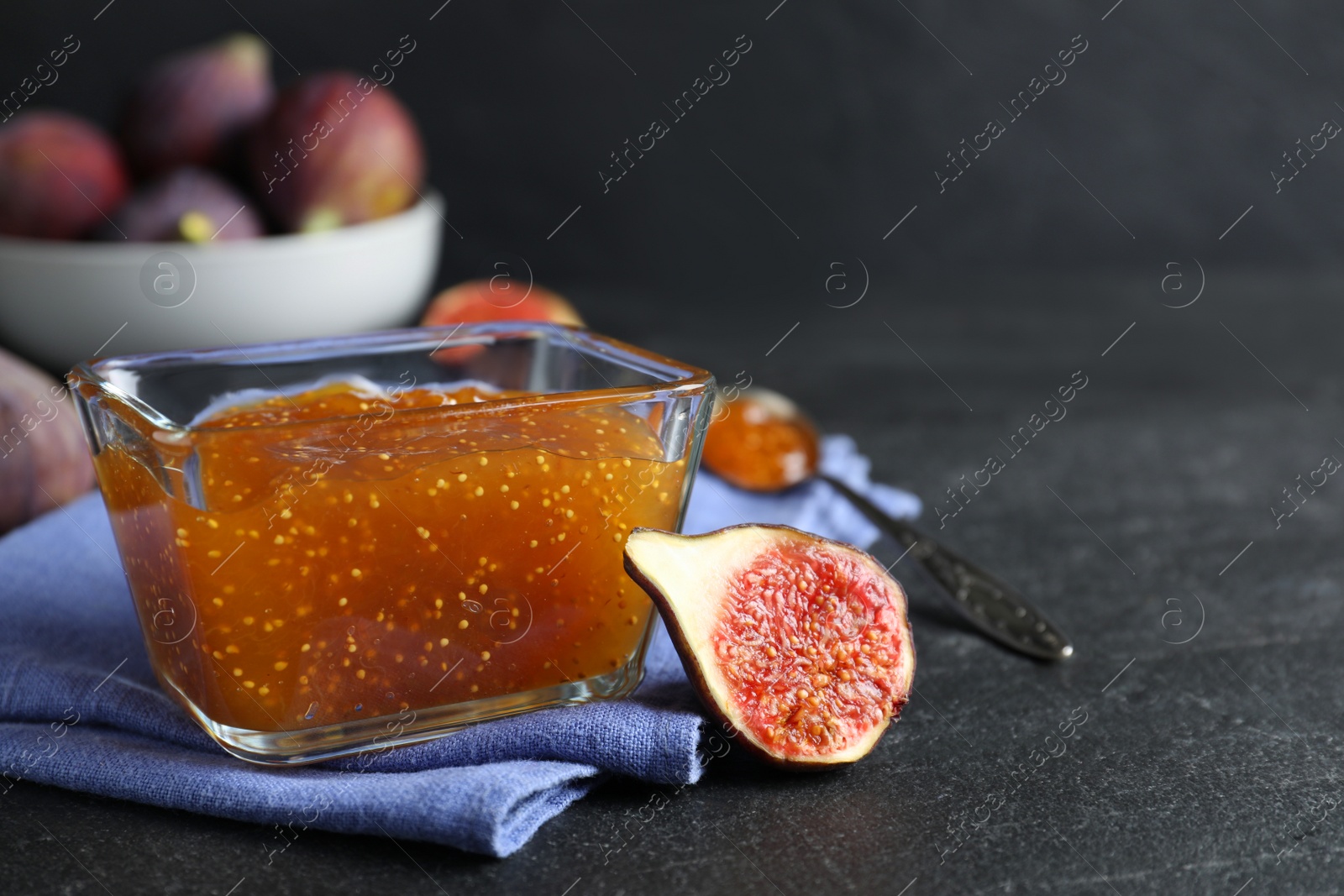 Photo of Delicious fig jam and fresh fruit on black table. Space for text