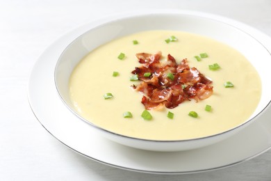 Tasty potato soup with bacon and green onion in bowl on white table, closeup