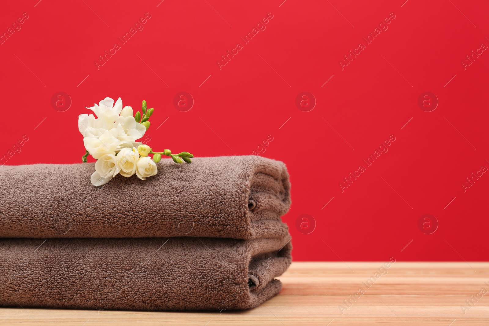 Photo of Soft clean towels with beautiful flowers on table against color background. Space for text