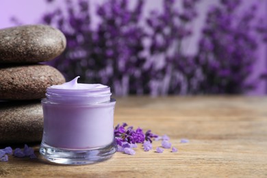 Photo of Stones, jar of cream and lavender flowers on wooden table. Space for text