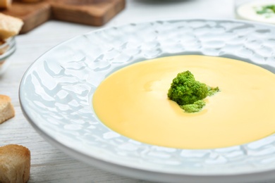 Photo of Bowl of cheese cream soup with broccoli served on white wooden table, closeup