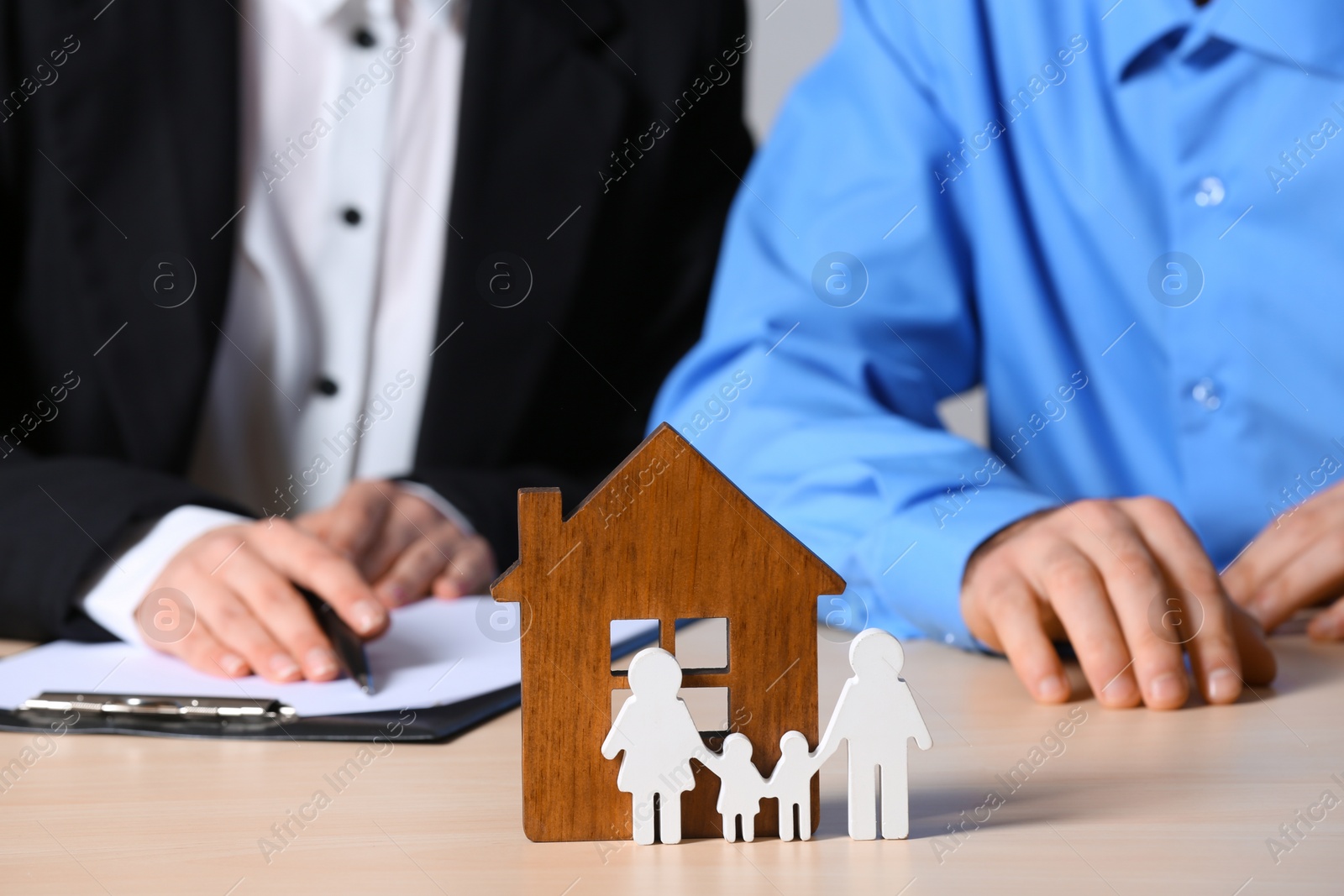 Photo of Real estate agent working with client at table, focus on house and family figures. Home insurance