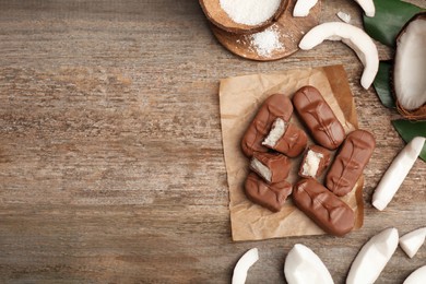 Photo of Delicious milk chocolate candy bars with coconut filling on wooden table, flat lay. Space for text