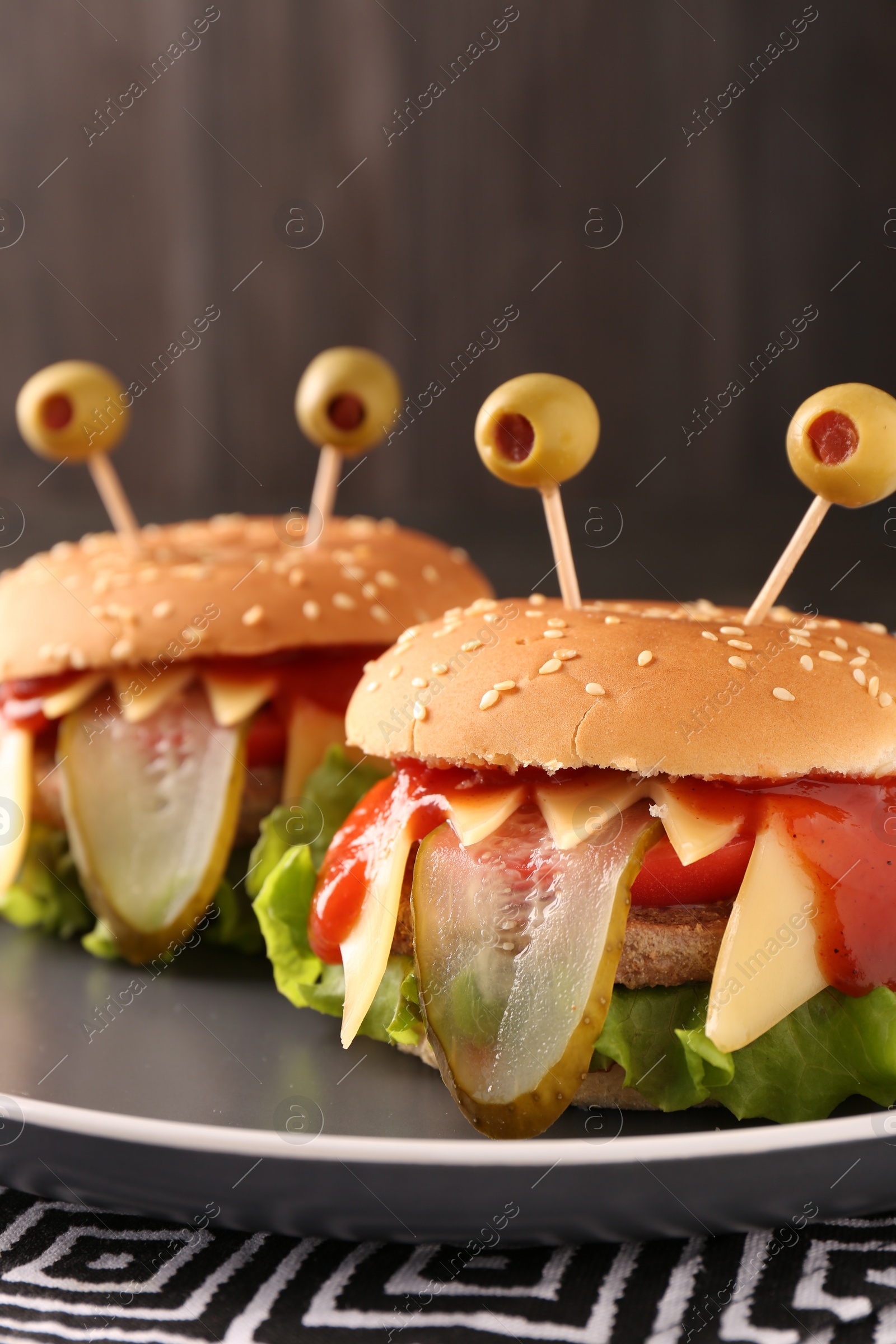 Photo of Cute monster burgers on table, closeup. Halloween party food