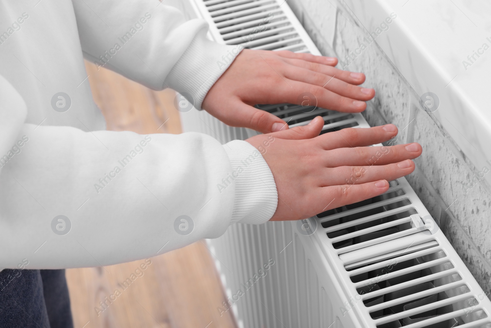 Photo of Girl warming hands on heating radiator indoors, closeup