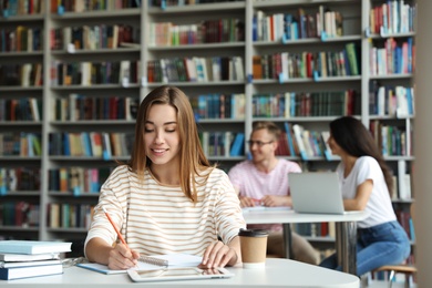 Photo of Young woman studying at table in library