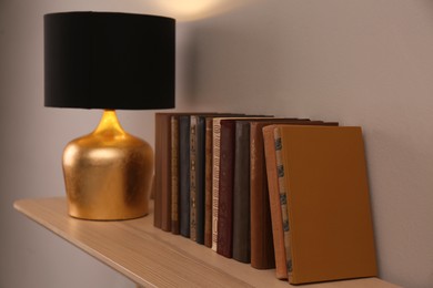 Photo of Wooden shelf with different books and lamp on light wall
