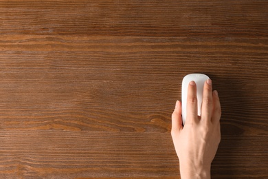 Woman using computer mouse on wooden background, top view. Space for text