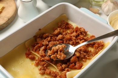 Photo of Cooking lasagna. Pasta sheets and minced meat in baking tray on white table, closeup