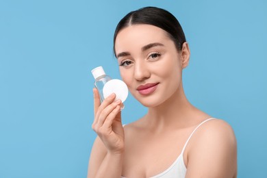 Photo of Beautiful woman with makeup remover and cotton pad on light blue background, space for text