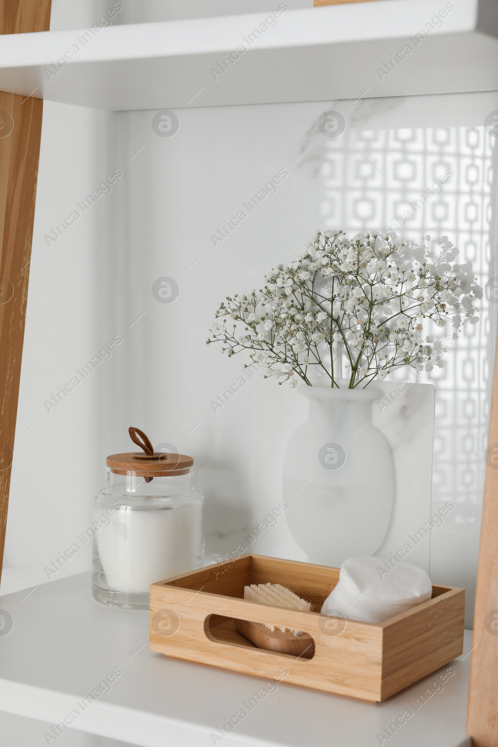 Photo of Silicone vase with flowers on white marble wall and shelving unit in stylish bathroom