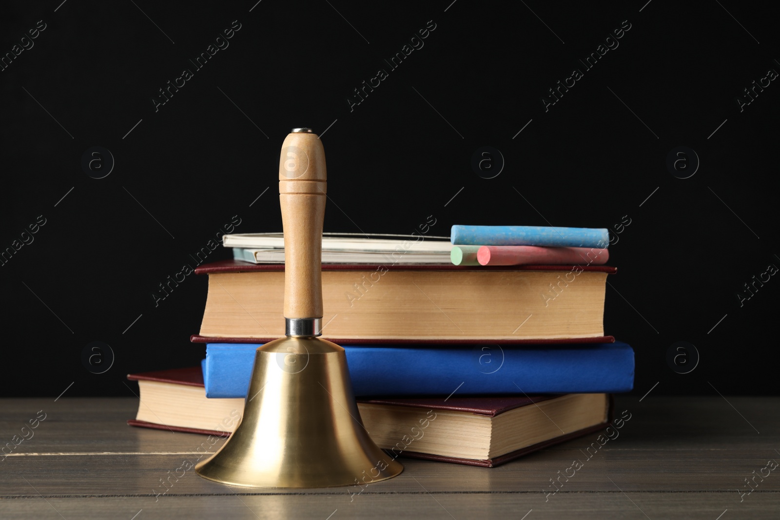 Photo of Golden bell, books and pieces of chalk on wooden table near blackboard. School days