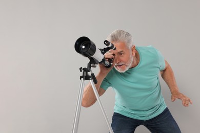 Senior astronomer looking at stars through telescope on grey background, space for text