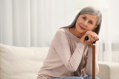 Mature woman with walking cane on sofa indoors