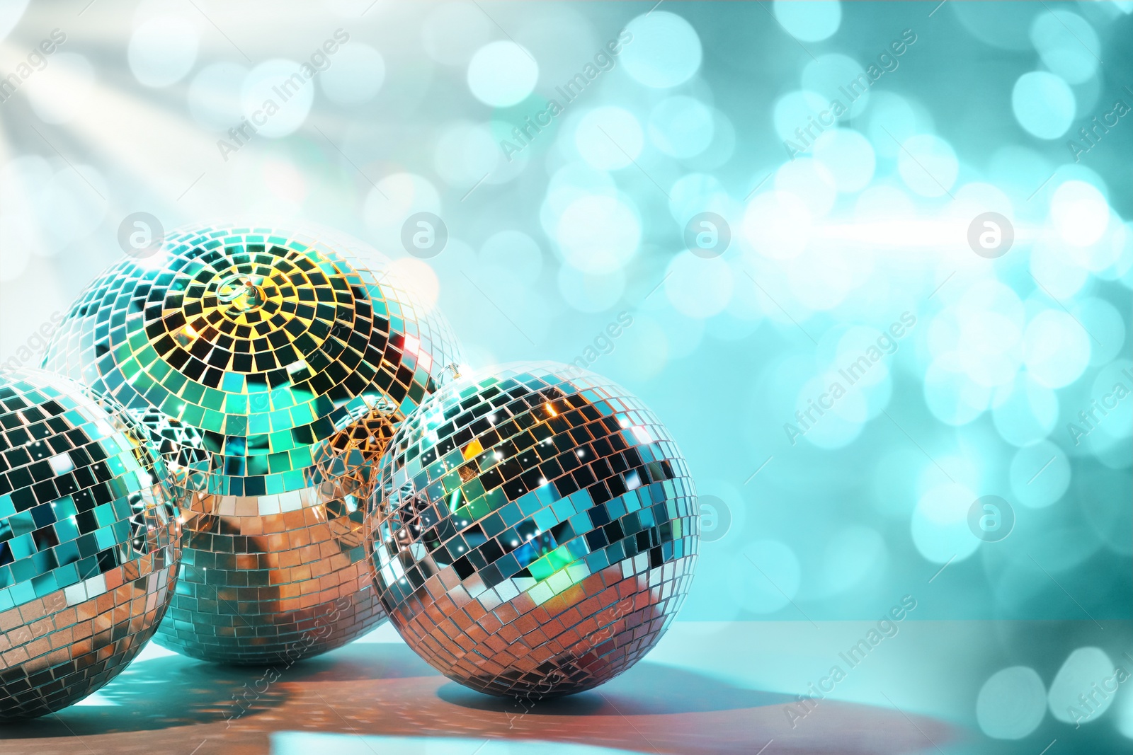 Image of Shiny disco balls on table against turquoise background with blurred lights, space for text. Bokeh effect