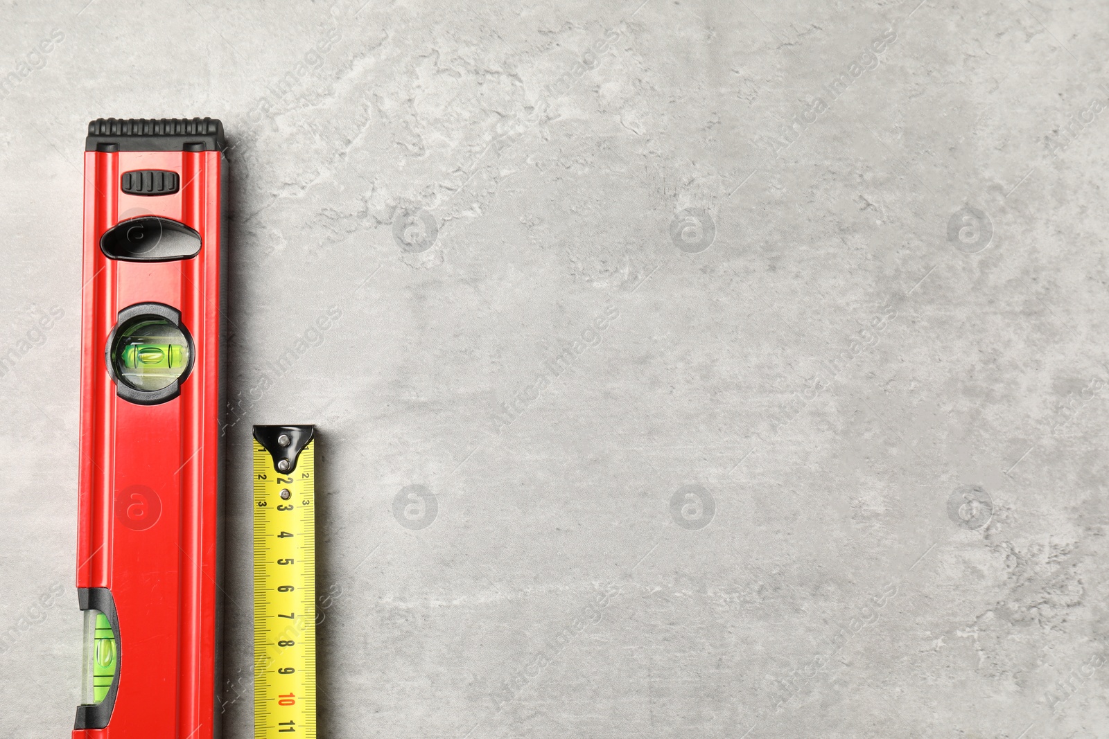 Photo of Building level and tape measure on grey table, top view. Space for text