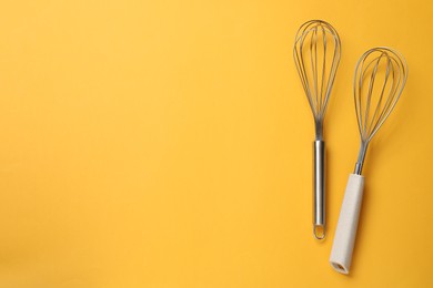 Two metal whisks on yellow background, top view. Space for text